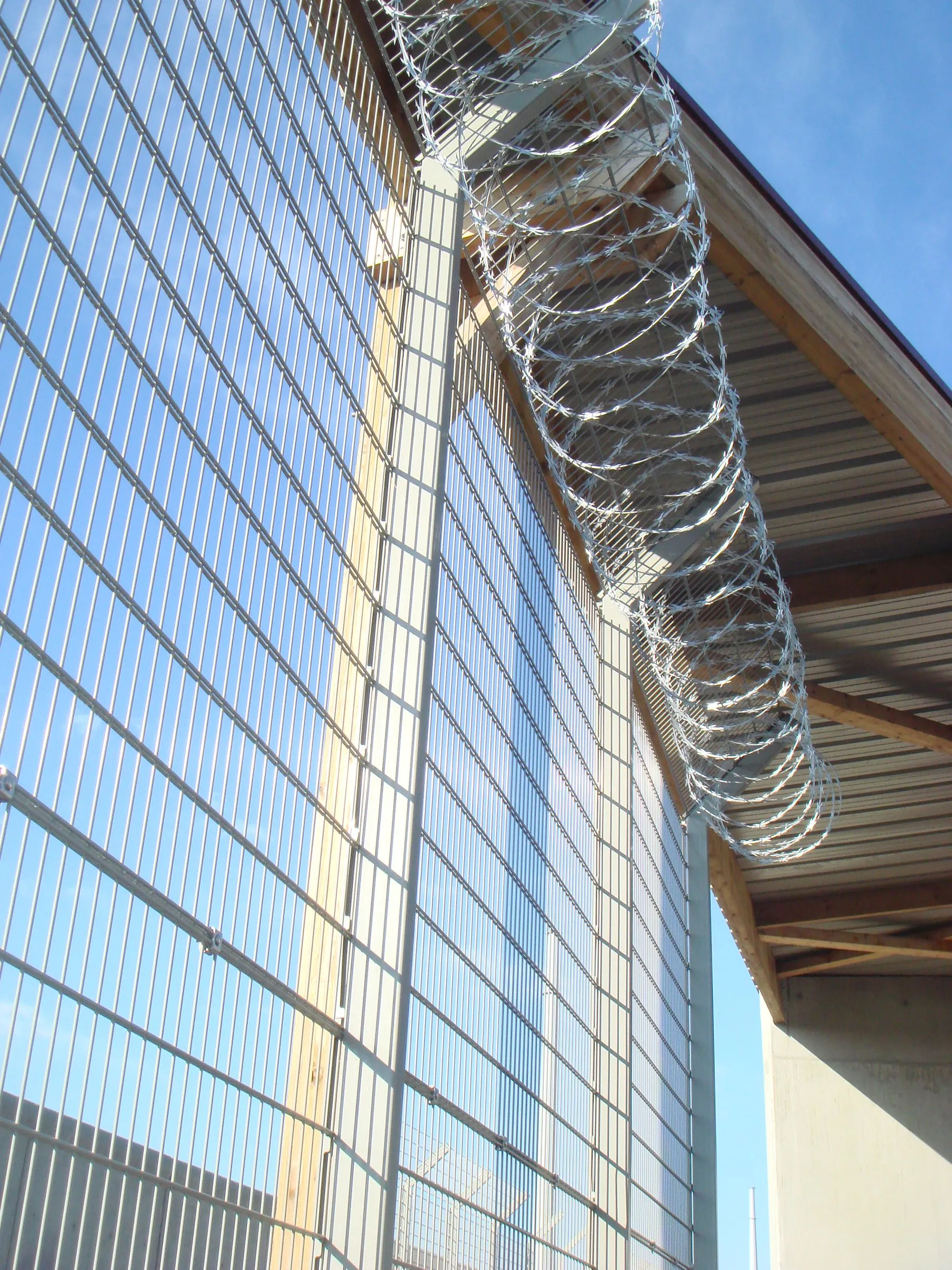 Clôture à mailles denses anti-escalade surmontée de concertina le long d'un bâtiment